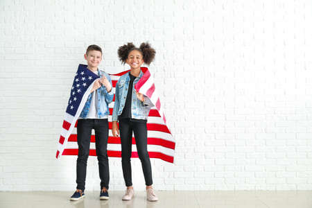 Cute children with national flag of USA near white brick wallの写真素材
