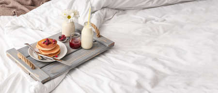 Tray with tasty breakfast on bed