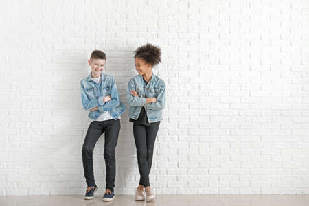 Stylish children in jeans clothes near white brick wall