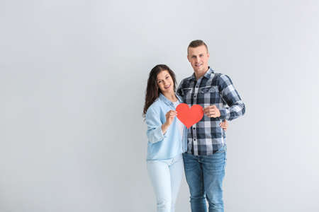 Adorable loving couple with paper heart on gray background