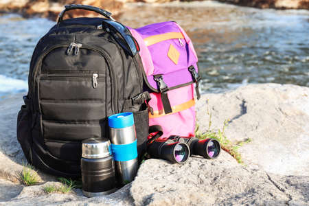 Tourist's backpacks with flask and binocular on rock near mountain streamの写真素材