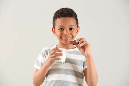 Cute African-American boy with glass of milk and cookie on white backgroundの写真素材