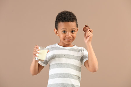 Cute African-American boy with glass of milk and cookie on color backgroundの写真素材