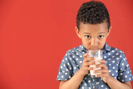 Cute African-American boy with glass of milk on color background