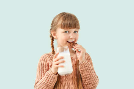 Cute little girl with glass of milk and cookie on light backgroundの写真素材