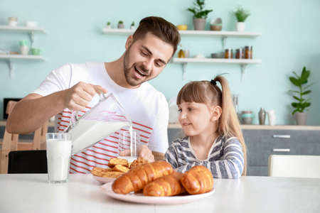 Young father with little daughter drinking tasty milk in kitchen at homeの写真素材