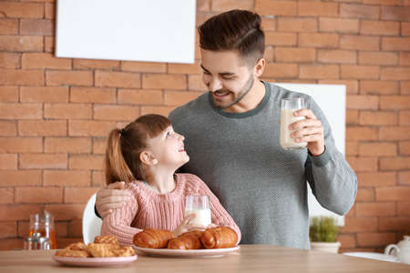Young father with little daughter drinking tasty milk in kitchen at homeの写真素材