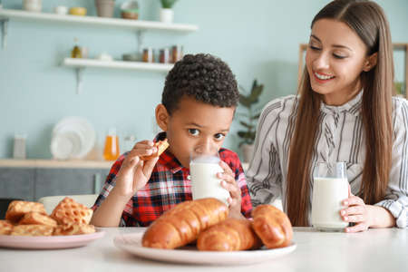 Young mother with adopted son drinking tasty milk in kitchen at homeの写真素材
