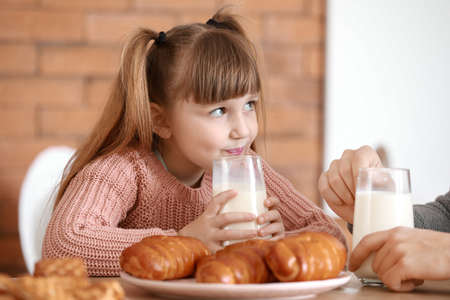 Little daughter drinking tasty milk in kitchen at homeの写真素材