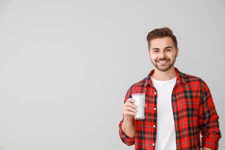 Handsome man with glass of tasty milk on light background