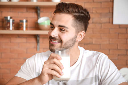 Handsome man drinking tasty milk in kitchen at homeの写真素材