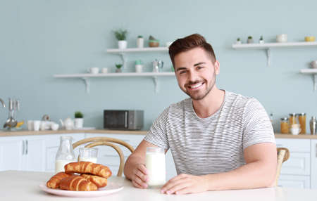 Handsome man drinking tasty milk in kitchen at homeの写真素材