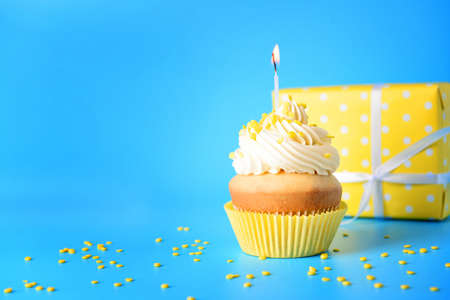 Tasty Birthday cupcake with gift box on color background