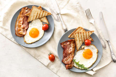 Plates with tasty grilled bread, fried eggs and bacon on tableの写真素材