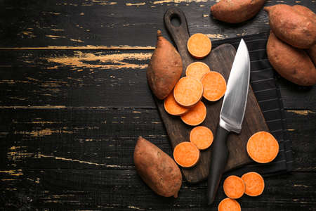 Cutting board and knife with raw sweet potato on wooden backgroundの写真素材