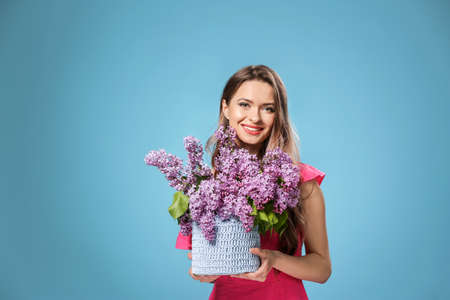 Beautiful young woman with bouquet of lilac flowers on color backgroundの写真素材