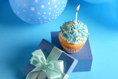 Tasty Birthday cupcake with gift box on color background