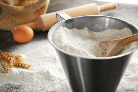 Measuring jug with flour on table, closeup