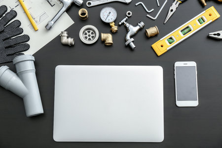 Modern laptop, mobile phone and plumbing items on dark backgroundの写真素材