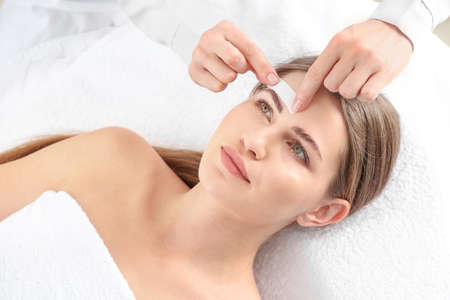 Young woman undergoing eyebrows epilation in beauty salon