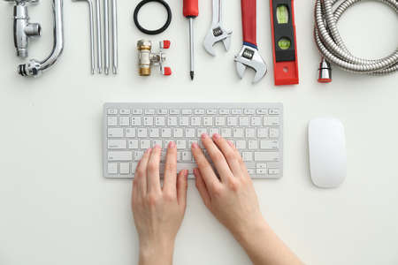 Plumbing tools and woman with computer keyboard on white background, top view
