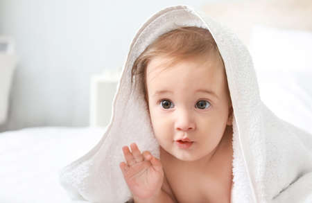 Portrait of adorable baby boy under towel on bedの写真素材