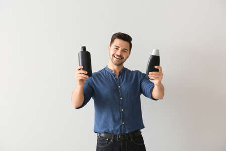 Handsome man with bottles of shampoo on light backgroundの写真素材