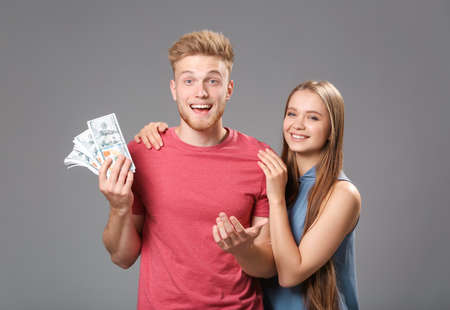 Happy couple with money on gray backgroundの写真素材