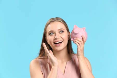 Happy woman with piggy bank on color background