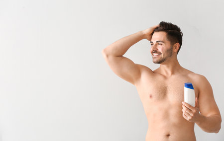 Handsome man with bottle of shampoo on light backgroundの写真素材
