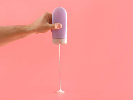 Male hand with bottle of shampoo on color background