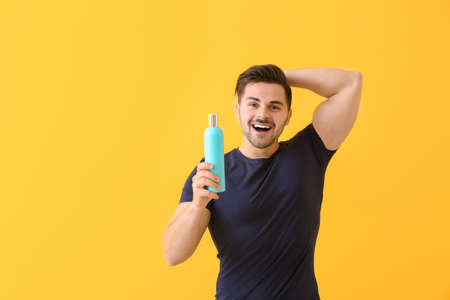 Handsome man with bottle of shampoo on color backgroundの写真素材