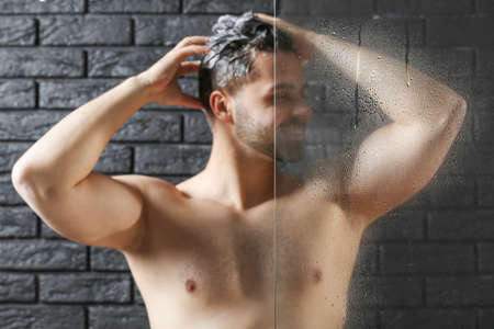 Handsome man washing hair on dark backgroundの写真素材