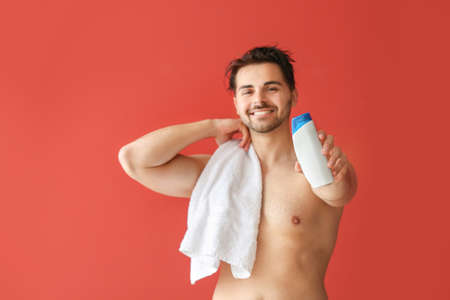 Handsome man with bottle of shampoo and towel on color backgroundの写真素材