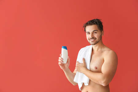 Handsome man with bottle of shampoo and towel on color backgroundの写真素材