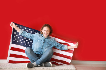 Happy young man with USA flag near color wall. Independence Day celebrationの写真素材