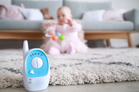 Modern baby monitor on floor in room with little child