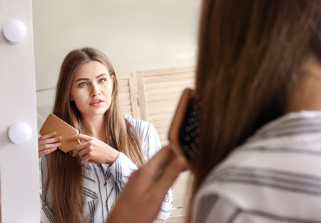 Young woman brushing hair near mirror in makeup roomの写真素材