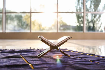 Rehal with open Koran on Muslim prayer mat indoorsの写真素材