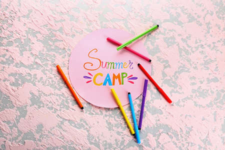 Sheet of paper with text SUMMER CAMP and felt-tip pens on color background