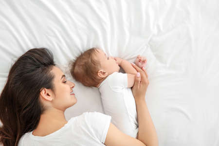 Happy mother with cute little baby lying on bedの写真素材