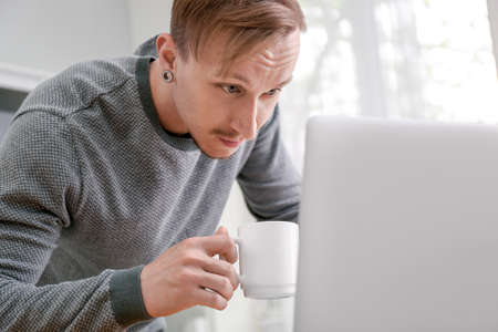 Handsome man working on laptop and drinking coffee at homeの写真素材