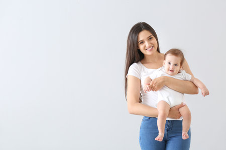 Happy mother with cute little baby on light backgroundの写真素材