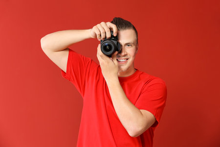 Handsome young man with photo camera on color backgroundの写真素材
