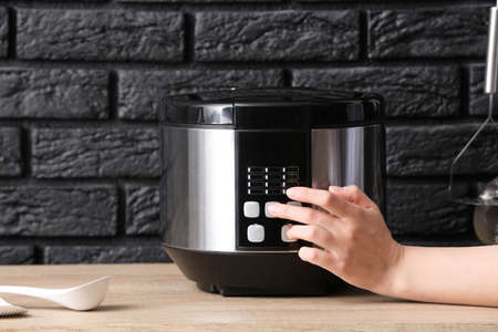 Woman switching on modern multi cooker on tableの写真素材