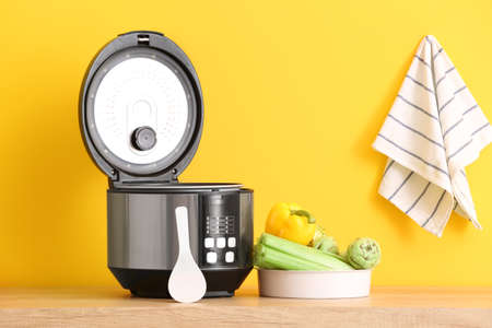 Modern multi cooker with vegetables on table against color backgroundの写真素材