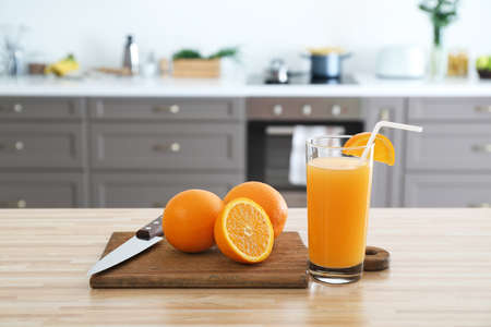 Cutting board with fresh oranges and juice in glass on table in kitchenの写真素材