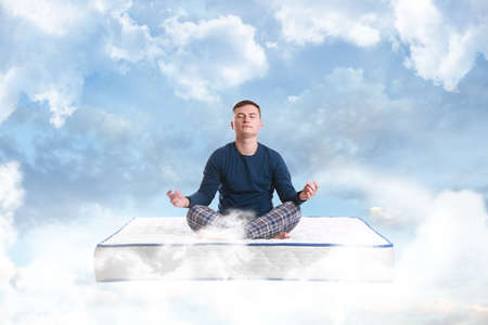 Young man meditating on mattress soft as clouds in blue skyの写真素材