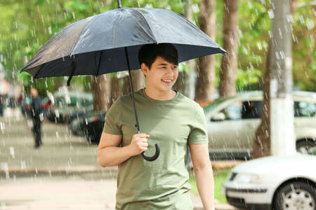 Handsome Asian man with umbrella outdoors on rainy dayの写真素材