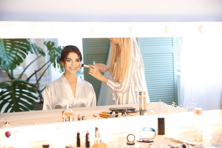 Reflection of professional makeup artist working with young bride at home